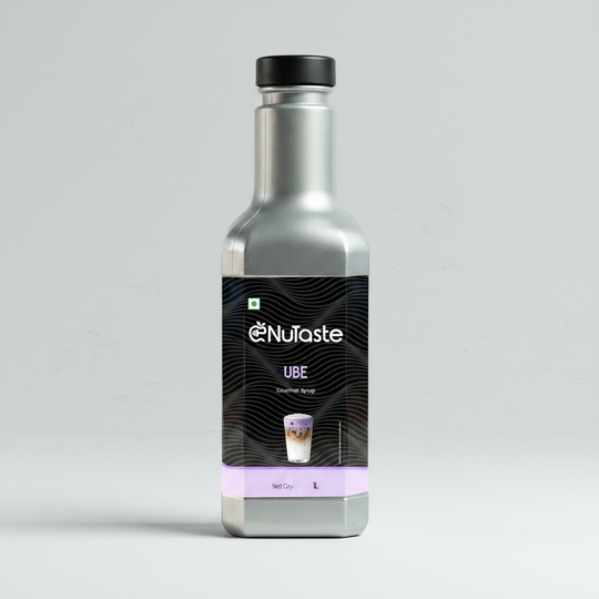 A bottle of NuTaste UBE Gourmet Syrup with a metallic silver bottle, black cap, and a black label featuring a purple bottom band, on a white background.